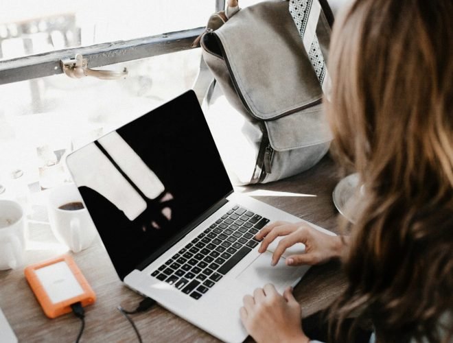 girl wearing grey long-sleeved shirt using MacBook Pro on brown wooden table