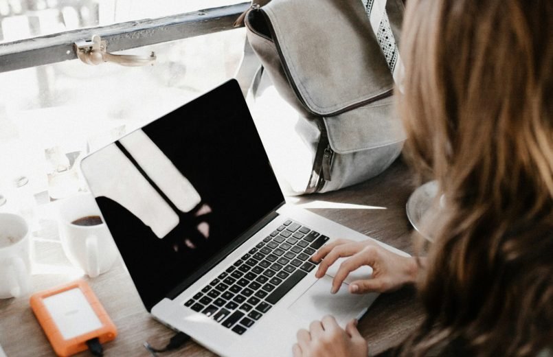 girl wearing grey long-sleeved shirt using MacBook Pro on brown wooden table